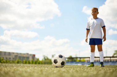 Top, ön plan odaklanmak yanındaki futbol alanında tek tip ayakta giyen boy gülümseyerek portresi