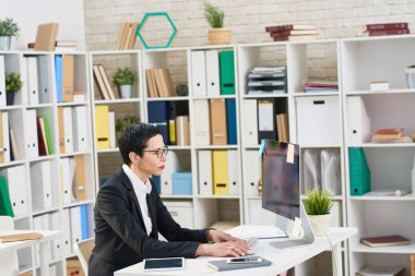 Kendine güvenen orta yaşlı iş kadını masada oturan ve istatistik verileri modern bilgisayar, iç arka plan üzerinde geniş Office Yardımı ile analiz gözlük profil görünümü