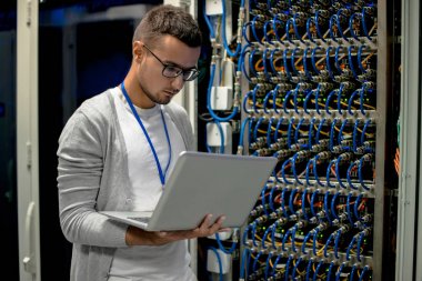 Yan görünümü süper bilgisayarla çalışırken sunucu kabine tarafından laptop ayakta kullanan genç adam portresi