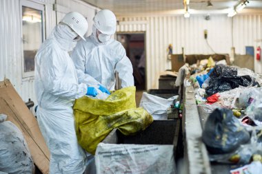 Geri dönüşümlü plastik ve karton işleme tesisi atık, Konveyör bant üzerinde sıralama yan görünüm portre biohazard giyen iki işçilerin uygun