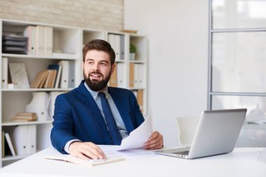 Mutlu bir şekilde uzağa modern ofis masasında çalışırken seyir gülümseyen başarılı sakallı işadamı portresi