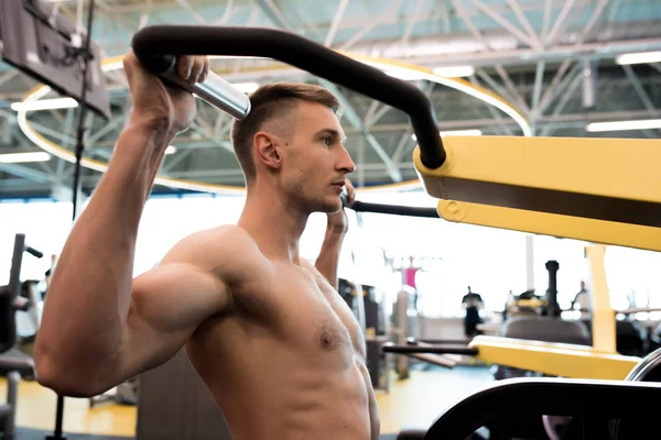 侧面图的英俊肌肉男子没有衬衫训练用运动机在现代健身房 — 图库照片