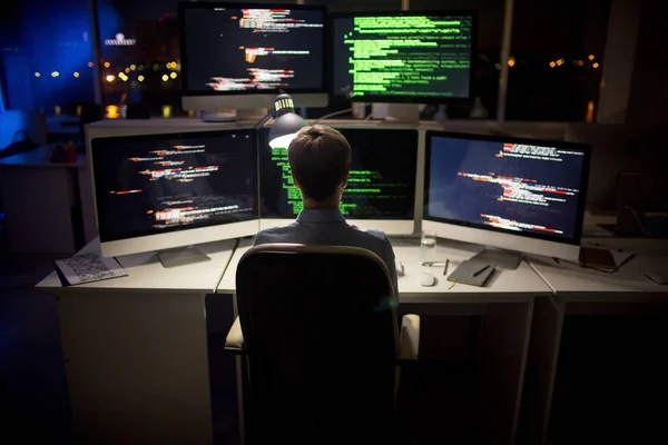 スタイリッシュな散髪コンピューターの前に座っていると 背景に薄暗いオープン プラン オフィスの内部コードを記述で一生懸命働くプログラマの背面します — ストック写真