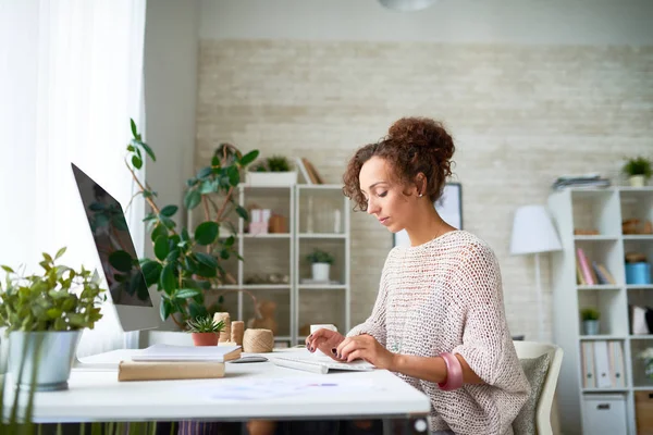 Side view portrait of beautiful mixed-race woman doing freelance work at computer in home office