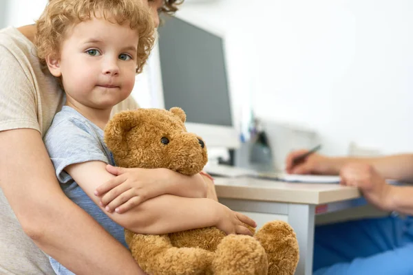 Portre portre sevimli çocuk annelerin kucak peluş oyuncak ayı oyuncak sarılma kadar onay bekliyor doktor ofisinde oturup...
