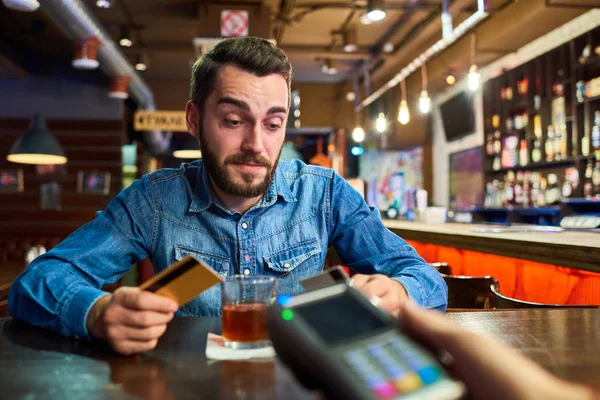 醉酒的年轻人的画像通过信用卡买饮料在酒吧与酒保递付款终端 — 图库照片