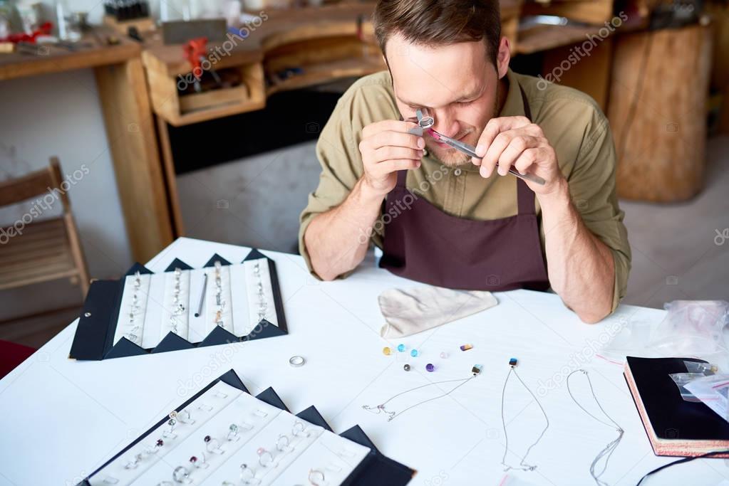 Portrait of young man inspecting jeweler with magnifying glass while appraising goods in pawn shop