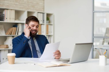 Telefonla konuşma ve modern ofis masasında çalışırken gülümseyen başarılı sakallı işadamı portresi