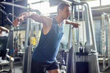 Sportif delikanlı kablo crossover makinasıyla yoğun egzersiz, modern bir spor salonu zemin üzerine iç yaparken