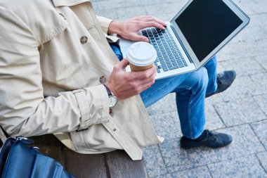 Sonbaharda kahve molası sırasında bankta oturan dizüstü kullanan tanınmaz halde genç adam portresi yüksek açı