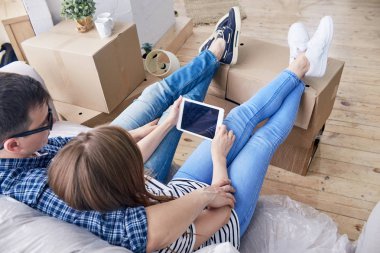 Arkadan görünüşü dijital tablet onların favori Tv dizi izlemek ve hareketli kutular içinde şeyler ambalaj mola sırasında rahat koltukta oturan güzel genç Çift.