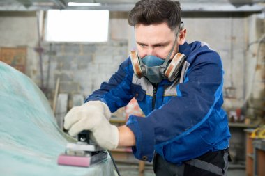 Portrait of man wearing respirator repairing boat in yacht workshop using electric polishing tool, copy space clipart