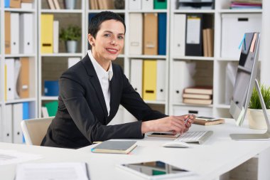 Bel öğe, dikey, ofis masa başında otururken çekici gülümseme ile kameraya bakarak çekici orta yaşlı girişimci