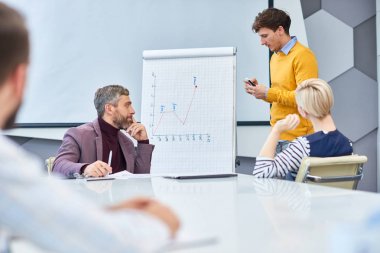Yakışıklı genç girişimci marker tahtaya ayakta ve geniş Yönetim Kurulu toplantısında çalışma yürütürken mali grafik çizim