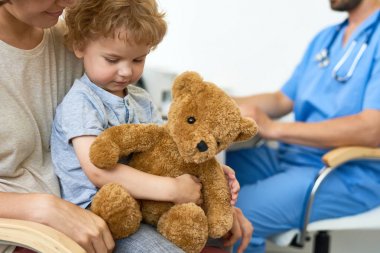 Annelerin kucak peluş oyuncak ayı oyuncak sarılma kadar onay bekliyor doktor ofisinde oturan sevimli küçük çocuk portresi