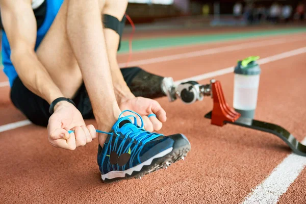 在现代体育场的跑道上 在运动靴上关闭无法辨认的截肢运动员绑鞋带 从实践中突围 — 图库照片