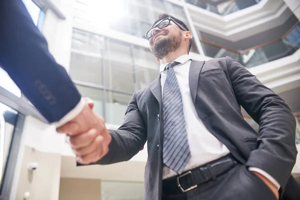 オフィス ロビー 低角度で立って握手と彼のビジネス パートナーを迎えるクラシック スーツを着て笑顔の中年起業家 — ストック写真