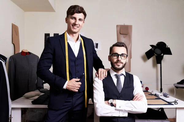 Portrait of two successful tailors posing in traditional atelier studio , looking at camera