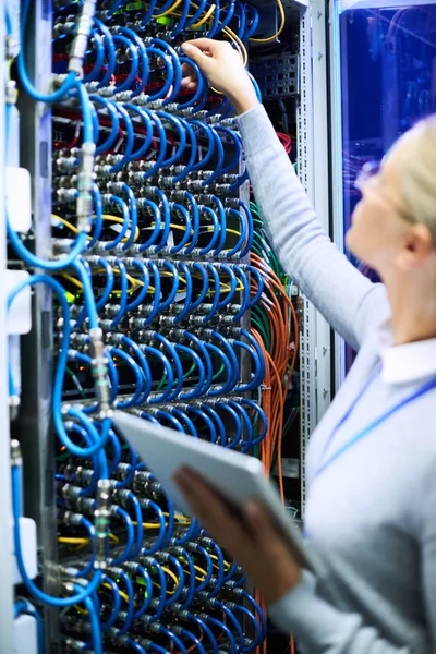 Young woman connecting wires in server cabinet while working with supercomputer in data center