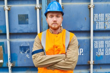 Bel öğe, dikey, kendine güvenen genç teknisyeni yansıtıcı yelek ve kask silah ile fotoğraflar için poz duran mavi konteyner depolama ünitesinde geçti
