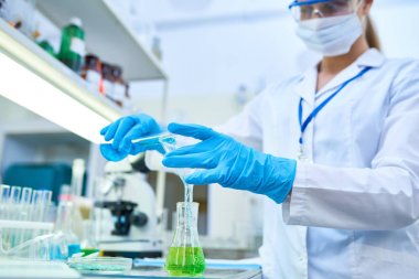 Koruyucu giyen kadın bilim adamı portresi tüpler tıbbi laboratuar kimyasallar okurken test, eller üzerinde odaklanmak için dökme renkli sıvı eldiven