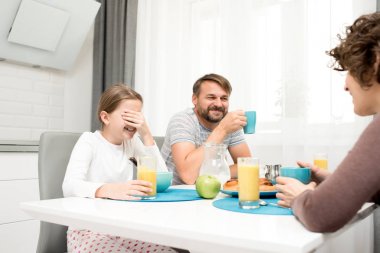 Mutlu bir şekilde evde kahvaltı tadını çıkarırken gülüyor kaygısız genç aile portresi, rahat mutfakta yemek masası sabah, portakal suyu içme oturmak