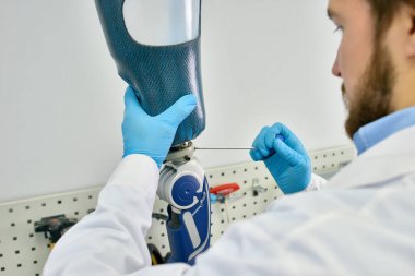 Portrait of prosthetic's technician making leg prosthesis sitting at desk in modern laboratory, checking it for quality and making adjustment clipart