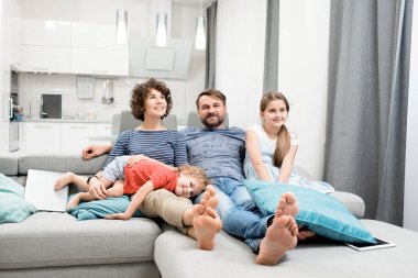 Dört rahat koltukta oturan ve arka plan üzerinde modern stüdyo dairenin iç onların en sevdiği Tv programı izlerken mutlu aile