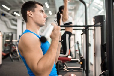İki kişi pencere, yakışıklı kaslı adam odaklanmak tarafından modern spor salonu makinelerde egzersiz yan görünüm