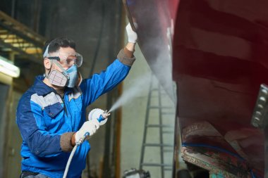 Side view portrait of worker wearing protective mask spray painting boat in yacht workshop  clipart