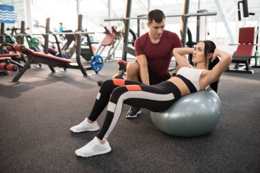 Genç kadının modern bir spor salonu, fitness Ball egzersizler yapması yardımcı kas Koç portresi