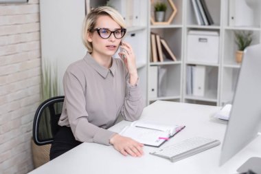 Sarışın başarılı işkadını cep modern ofis masasında oturan ve istemciye konuşurken telefonla konuşan portresi