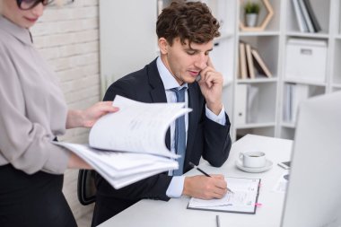 Resepsiyon ofiste çalışan, telefonla konuşma, notlar ve sekreter masasının tarafından ayakta ile bilgisayar kullanarak meşgul genç Yöneticisi portresi