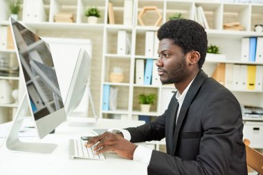 Masada oturan ve bilgisayar, iç arka plan üzerinde modern ofis yardımıyla umut verici proje üzerinde emin Afro-Amerikan Yöneticisi görünümünü profili