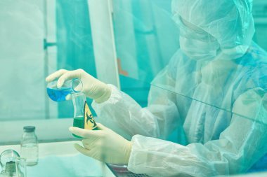 Yan görünümü biohazard malzemeleri ve tıbbi araştırma laboratuvarında virüs çalışma maske ve koruyucu giysi giymiş kadın bilim adamı portresi