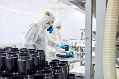 Tulum ve hap, arka plan üzerinde modern ilaç Fabrikası'nın iç şişeyle tartmak için elektronik ölçeği kullanarak Trikotaj eldivenler giymiş işçilerin grup