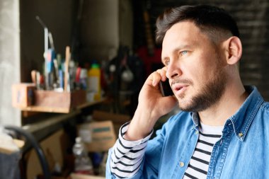 Ahır gibi atölye dururken telefonla konuşan yakışıklı olgun adam baş ve omuzlar portresi