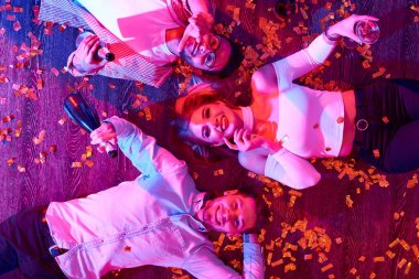 Konfeti ve serpantin arasında katta yalan ve harika ev partisi sırasında kameraya bakarak gülümseyen üç genç insanların Üstten Görünüm