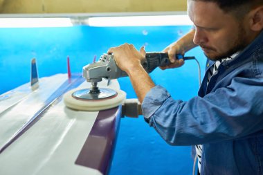 Modern işçi özel sörf tahtası atölyesinde elektrik polisaj aracıyla parlatma yan görünüm