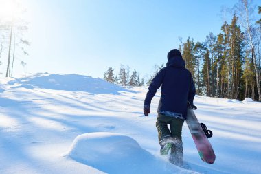 Arkadan görünüşü serbest gitmek için karlı tepeye çalışan genç snowboard ormanda vahşi yolda sürme