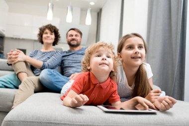İki çocukla birlikte kız ve erkek kardeşim ön planda odak oturma odasında kanepede oturup Tv izlerken mutlu bir aile portresi