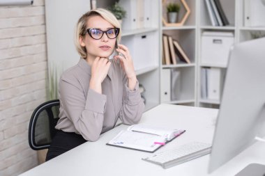 Sarışın başarılı işkadını modern ofis masasında oturan ve uzak ikindilerde seyir telefonla konuşan portresi