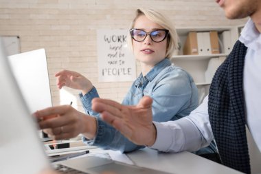 Ofiste sarışın kadın iş ortağı ile tartışırken odak masada oturan dizüstü kullanan iki gençlerin portresi