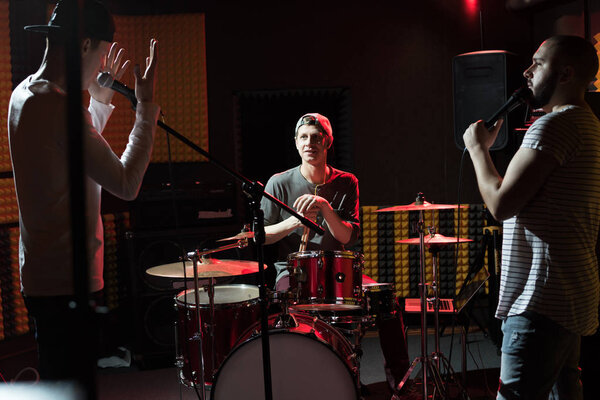 Портрет современной хип-хоп группы, репетирующей в студии звукозаписи, освещенной тусклыми огнями во время работы над новым альбомом
