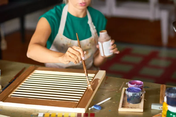 Close up of young woman enjoying work in art studio painting shutters with bronze paint, making DIY interior decoration