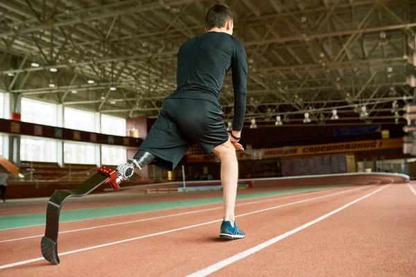 Motivational image of young amputee athlete warming up on running track in modern indoor stadium