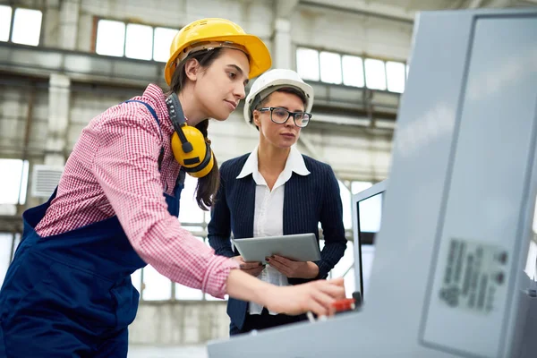 マシン単位のコントロール パネルによって立っている近代的な工場で働く Hardhats を着た つの若い女性の低角度の肖像画 — ストック写真