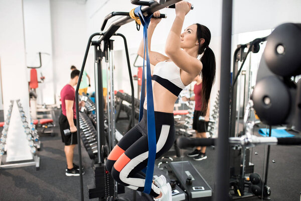 Side view of young woman exercising on machines in modern gym