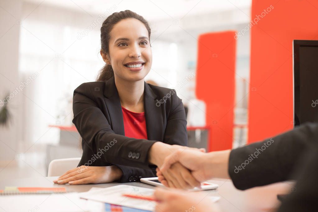 Portrait of smiling mixed-race businesswoman shaking hands with partner after closing successful deal during meeting in modern office