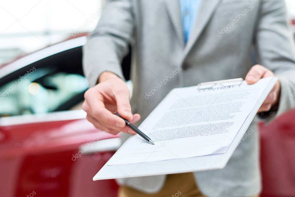 Close up view  portrait of unrecognizable car salesman handing purchase contract to client buying brand new car in luxury showroom